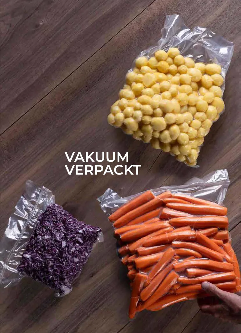 Vakuumverpacktes Bündel aus rohem Gemüse: geschälte Baby-Erdäpfel, ganze Karotten und gehobeltes Rotkraut.
